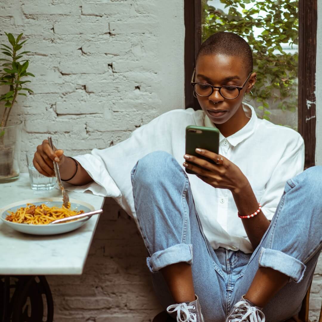 Woman eating pasta while scrolling phone.