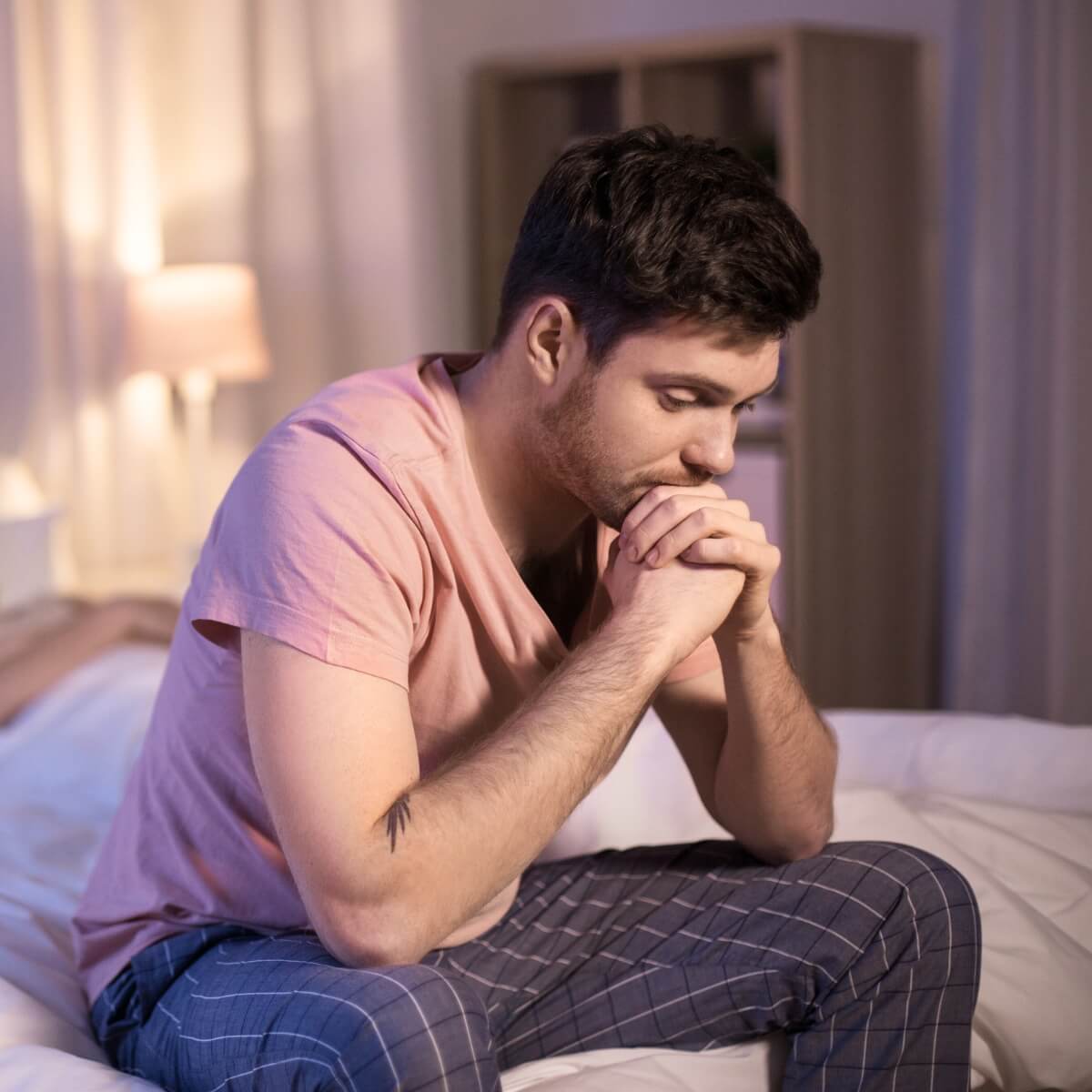 Man sitting on bed looking contemplative