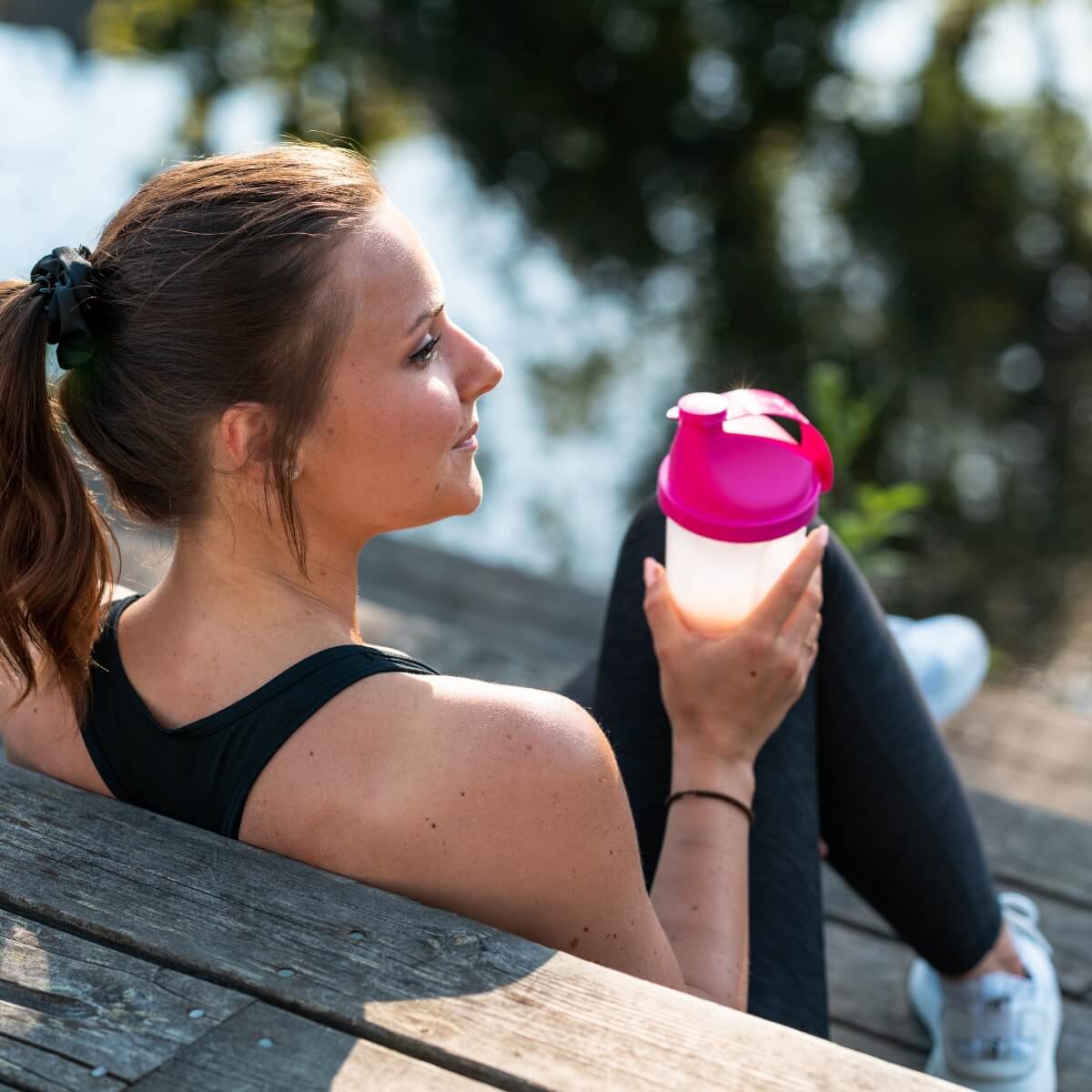 girl sitting on a dock holding a protein shake after workout