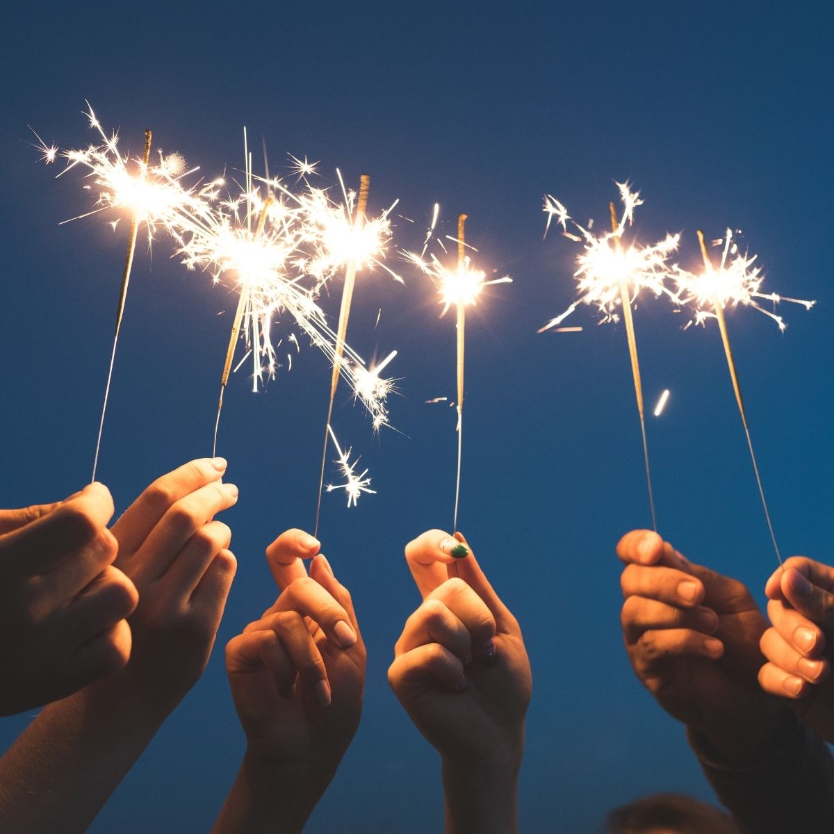 Hands holding sparklers against a dark blue evening sky, celebrating New Year’s goals and aspirations with a festive and hopeful atmosphere.