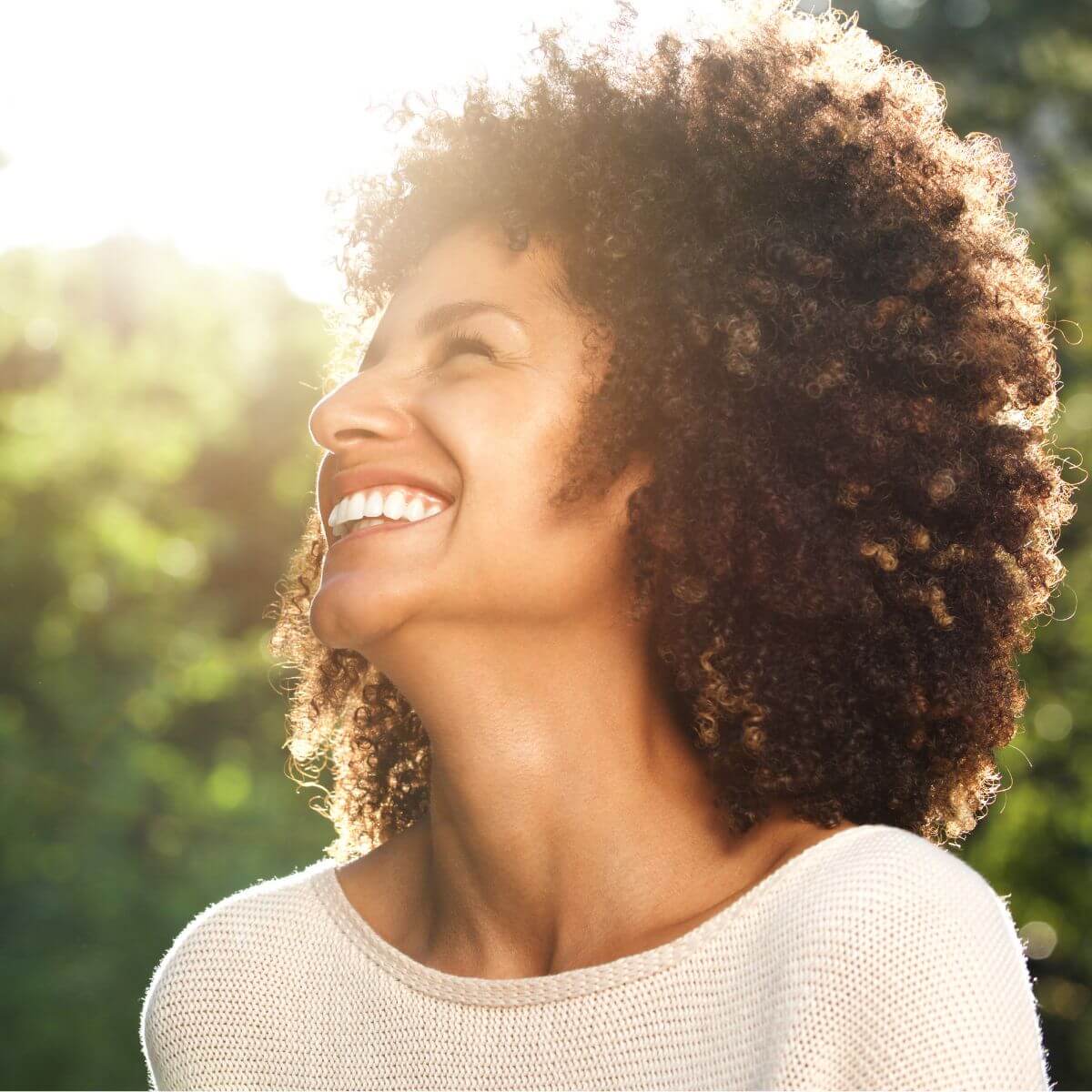 Woman with curly afro smiling into the sun.