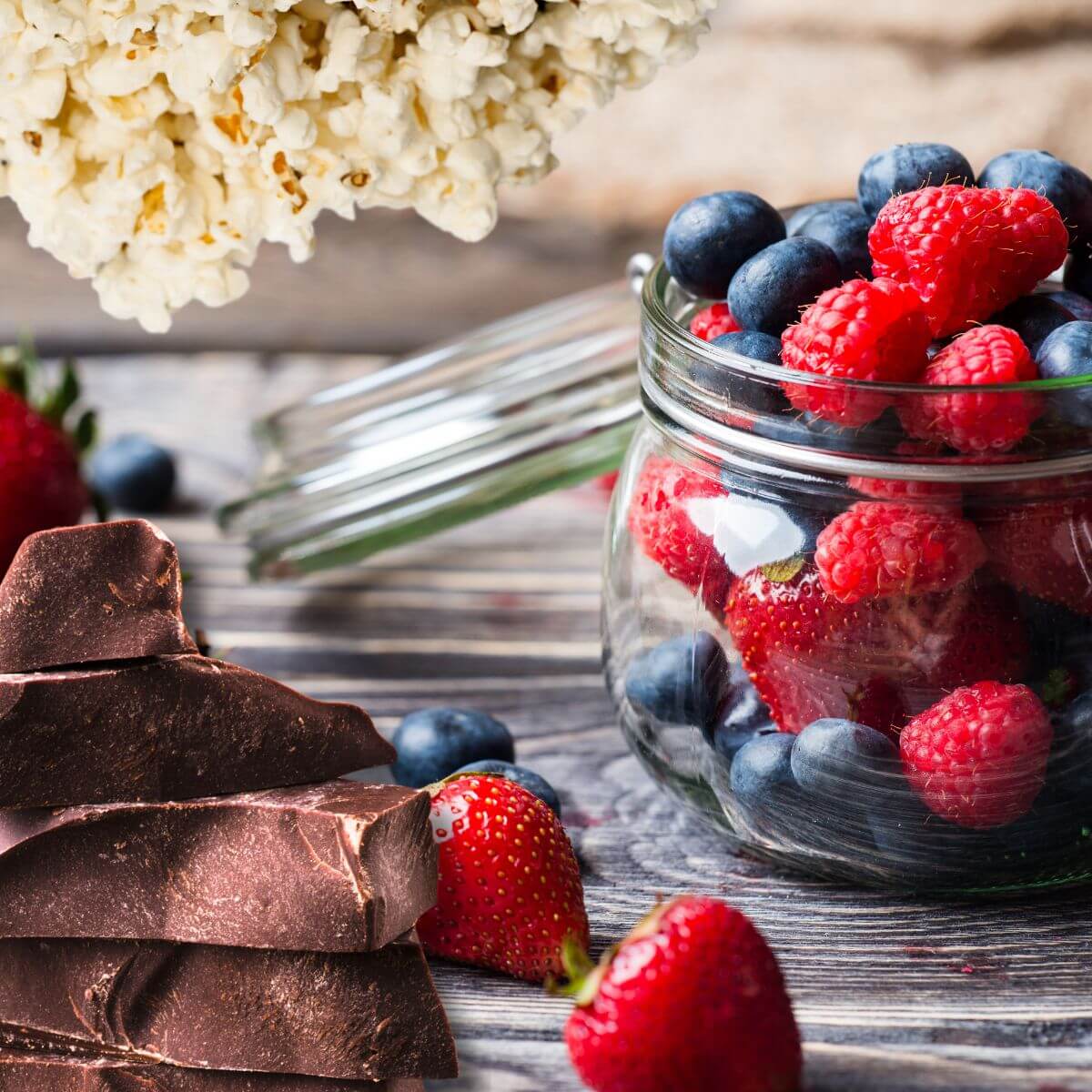 a montage of low sugar snacks including popcorn, berries and dark chocolate